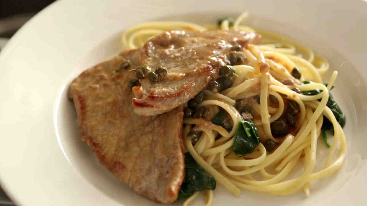 A mouthwatering image of Veal Piccata, glistening with lemon sauce and capers.