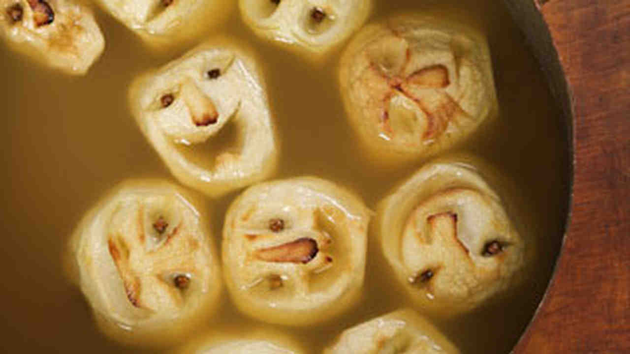 Peeled apples with faces, floating in a pot of cider.
