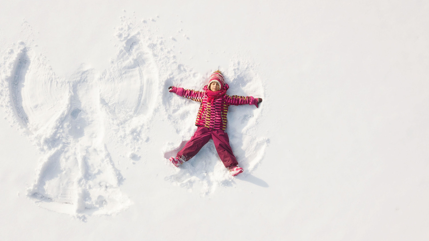 child in pink coat making snow angel