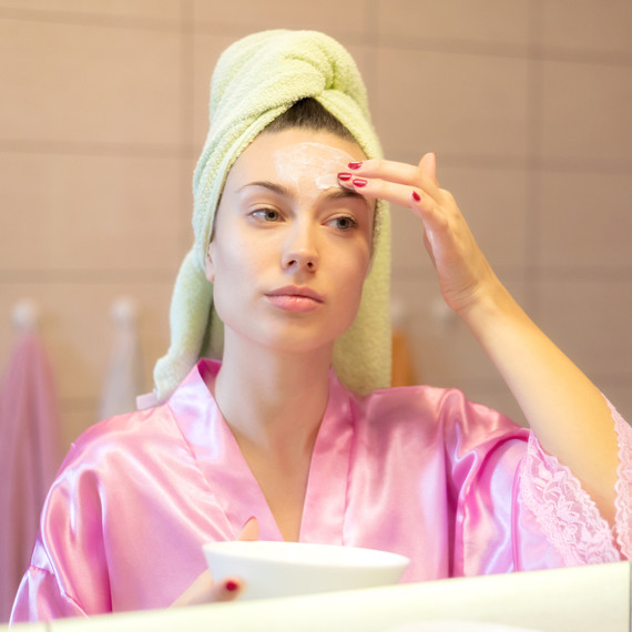 A woman applies face cream while looking in a mirror. A woman applies face cream while looking in a mirror.