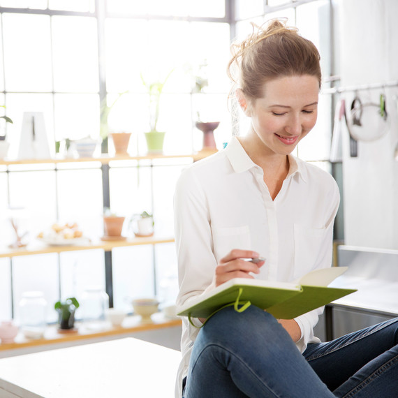 woman writing in green notebook with wall of plants in background woman writing in green notebook with wall of plants in background