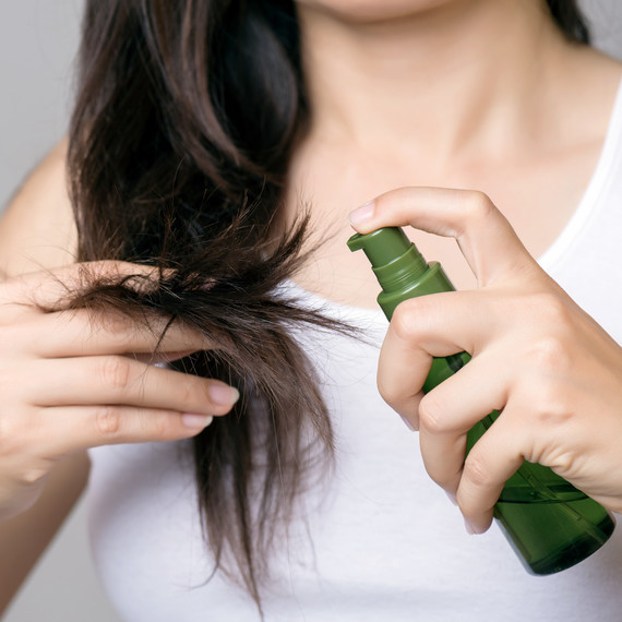 woman spraying oil on her hair ends woman spraying oil on her hair ends
