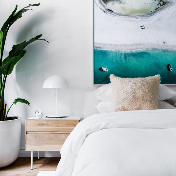 neutral bedroom with palm tree and abstract oceanic photograph above bed