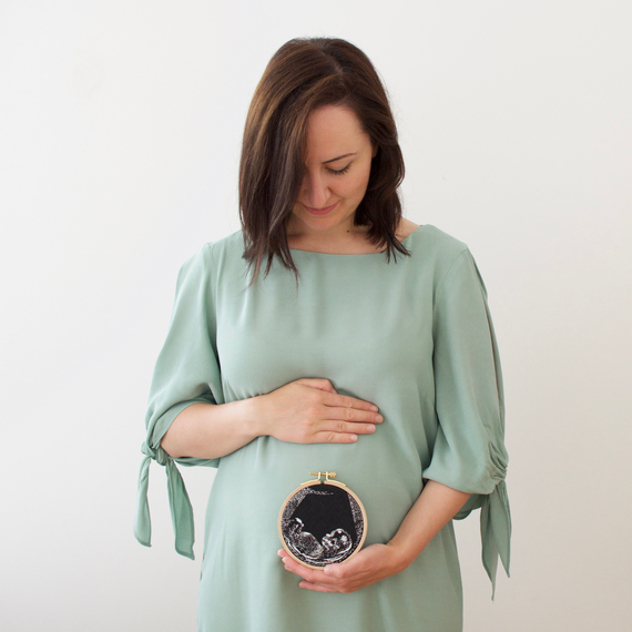 A woman holds an embroidery hoop with her ultrasound photo. A woman holds an embroidery hoop with her ultrasound photo.