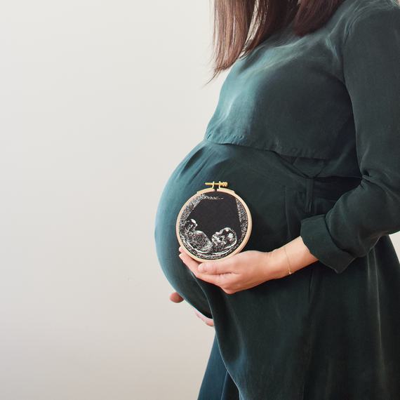 A woman holds an embroidery hoop with her ultrasound photo. A woman holds an embroidery hoop with her ultrasound photo.