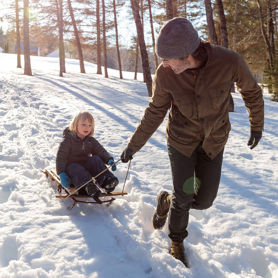 man pulls child on wooden sled across snow man pulls child on wooden sled across snow