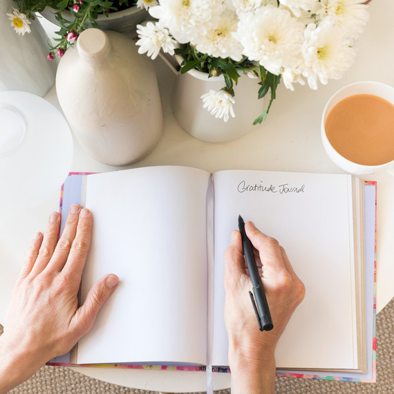 hands writing in journal on table with coffee cup and flowers hands writing in journal on table with coffee cup and flowers