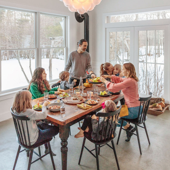 family eating dinner at vintage farm table near wood-burning stove family eating dinner at vintage farm table near wood-burning stove