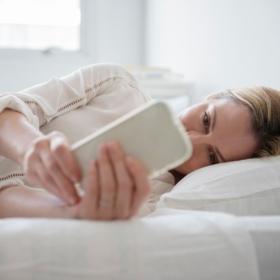 woman lying in bed looking at cell phone woman lying in bed looking at cell phone